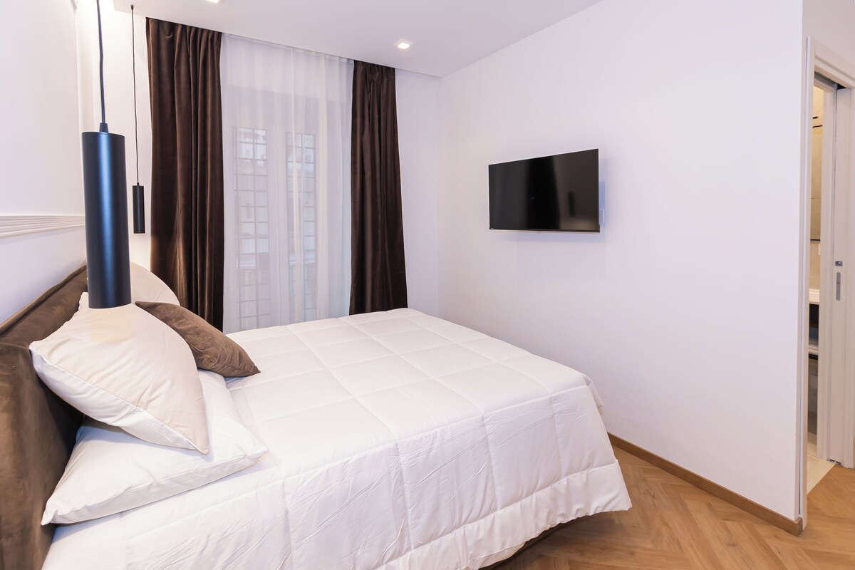 Habitación de hotel con cama, televisor de pantalla plana montado en la pared y ventana con cortinas.