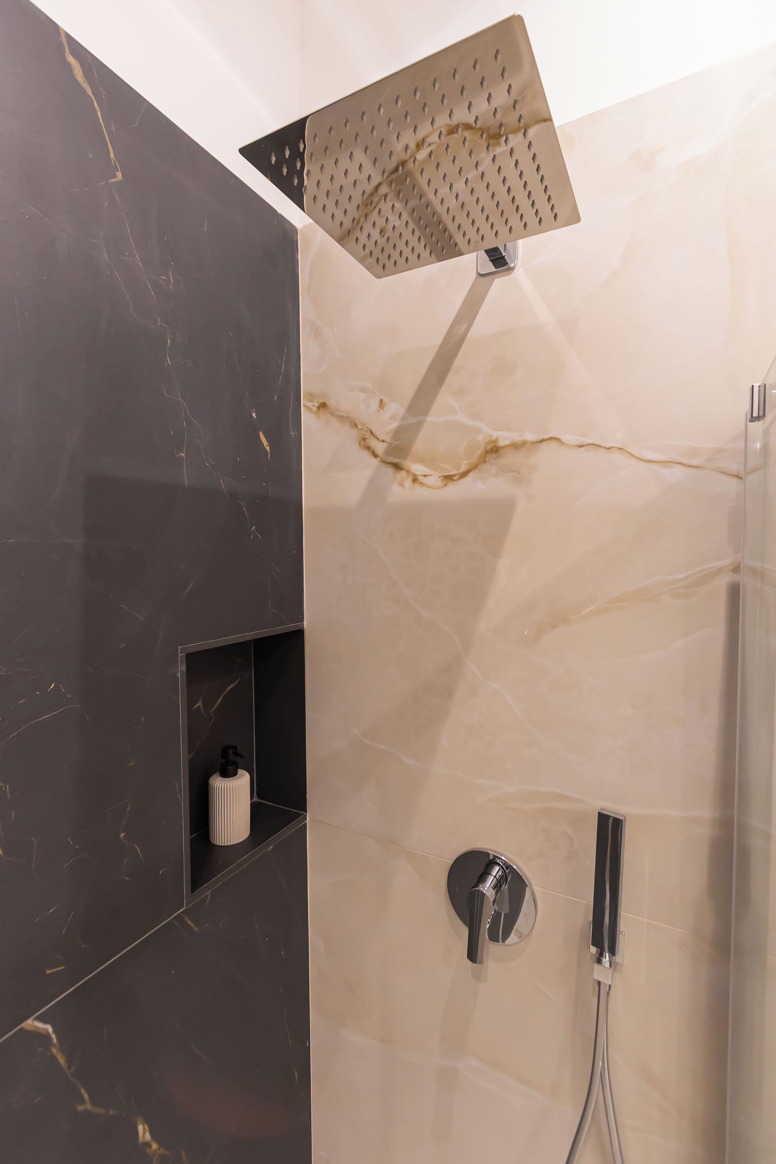 Een moderne douche met een vierkante douchekop, een handdouche en een bedieningspaneel aan de muur.