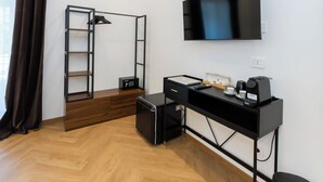 A modern room with a desk, a flat-screen TV, a ladder, a safe, and a coffee machine.
