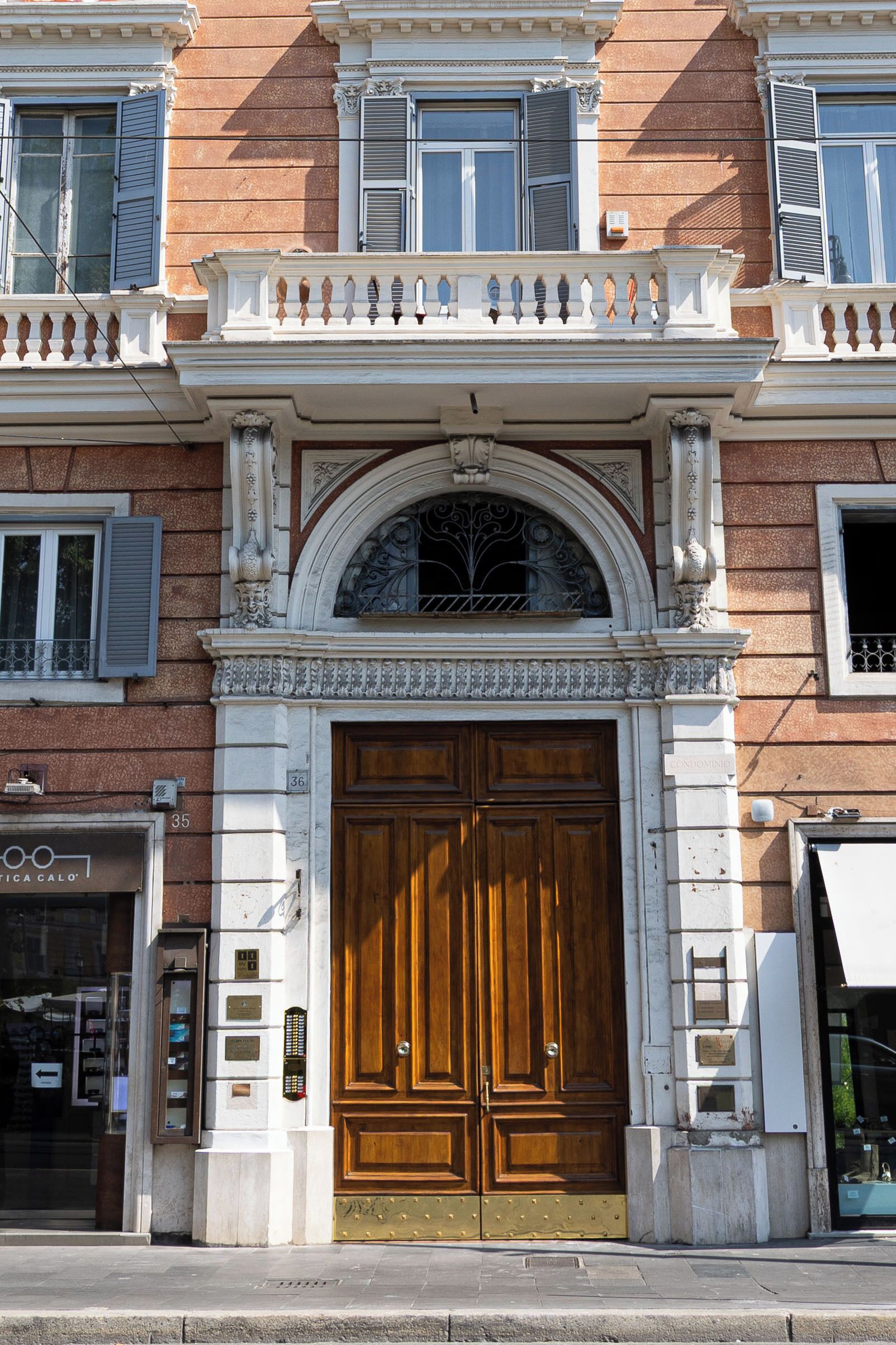 A building facade with a large wooden double door, a balcony with ornate balustrade, and a window with decorative ironwork.