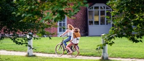 Dos personas montando en bicicleta por un sendero, con un edificio al fondo.