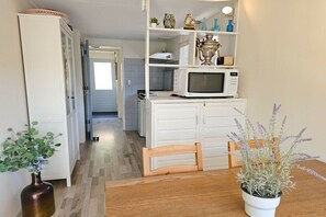 A kitchen with white cabinets, a microwave, and a wooden dining table with a potted plant. - OK11 Bungalow Oostkapelle (Oostkapelle)