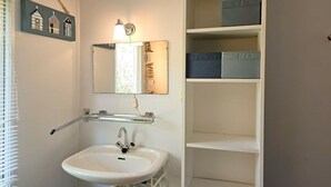 Un baño con un lavamanos blanco, un espejo y una estantería con cajas de almacenamiento.