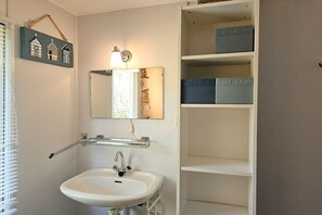 A bathroom with a white sink, a mirror, and a shelf unit with storage boxes. - OK11 Bungalow Oostkapelle (Oostkapelle)