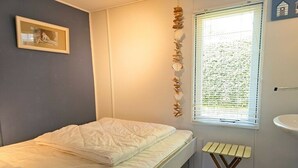 Un dormitorio con cama, una ventana con persianas, un taburete pequeño y un cuadro en la pared.