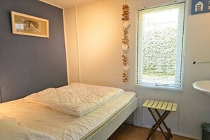 A bedroom with a bed, a window with blinds, a small stool, and a framed picture on the wall. - OK11 Bungalow Oostkapelle (Oostkapelle)