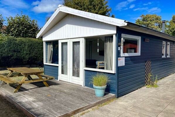 A small, single-story building with a covered patio area, a wooden picnic table, and a potted plant. - OK11 Bungalow Oostkapelle (Oostkapelle)