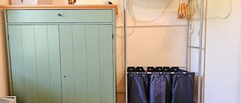 A room with a green wardrobe, a metal drying rack with clothes, and a small stool.
