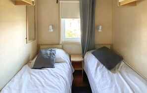 A small, narrow room with two single beds, a window with curtains, and a small table. - 2 bedroom gorgeous home in Färjestaden (Färjestaden)