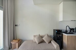 Una habitación de hotel moderna con cama, una mesita auxiliar, cafetera y una cocina integrada.