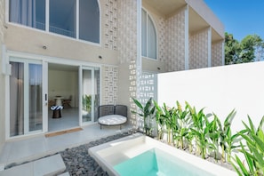 Un área de piscina moderna al aire libre con un jacuzzi, rodeada por un muro blanco y follaje.
