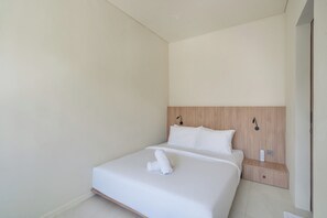 Un dormitorio minimalista con una cama individual, cabecera de madera, mesita de noche y una lámpara de pared.