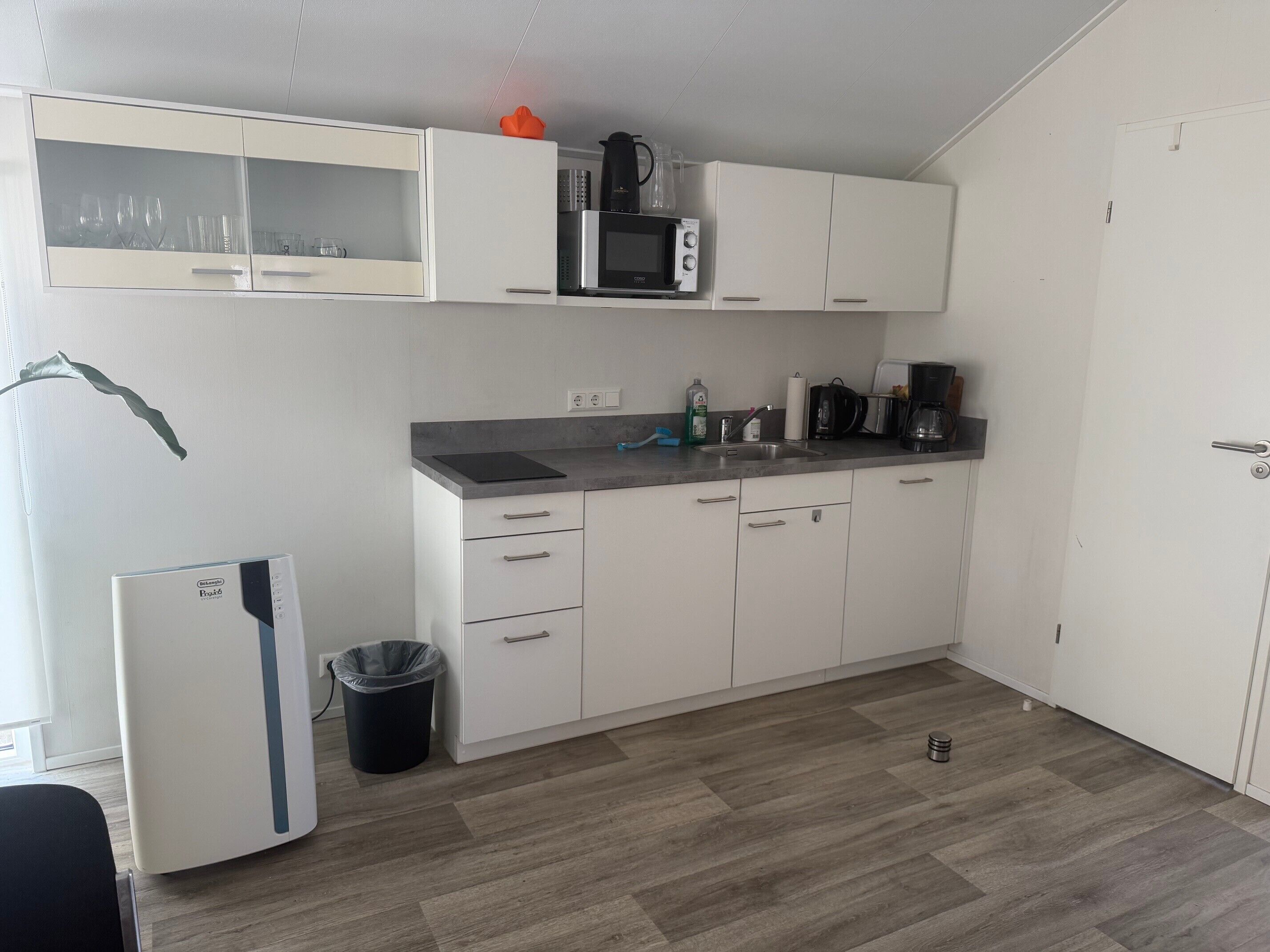 A compact kitchen with white cabinets, a microwave, a coffee maker, and a trash bin.
