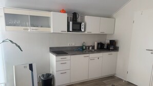Een kleine keuken met witte kasten, een magnetron, een koffiezetapparaat en een prullenbak.