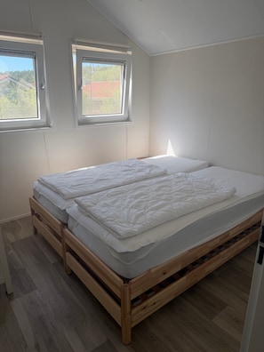 A bedroom with a wooden bed frame, two windows, and a view of the outside. - Tiny Home “House K116” with Private Terrace, Wi-Fi & Air Conditioning (Röbel)