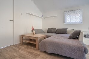 A modern, well-lit bedroom with a large bed, a small table, and a window with patterned curtains. - Tiny Home “House K116” with Private Terrace, Wi-Fi & Air Conditioning (Röbel)
