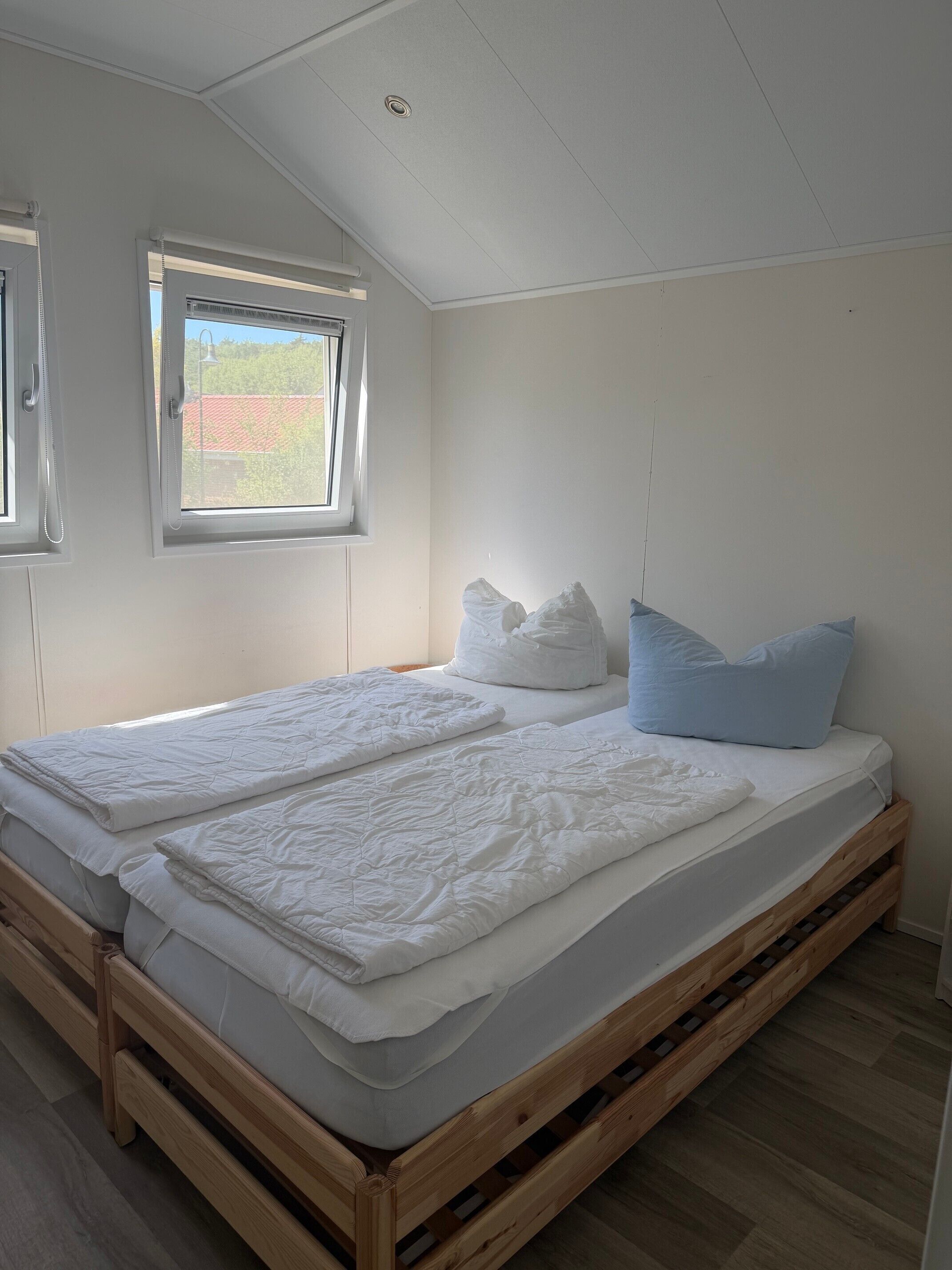 A bedroom with a wooden bed frame, two windows, and a view of the outside.