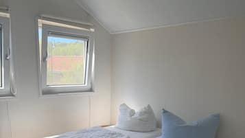 A bedroom with a wooden bed frame, two windows, and a view of the outside.