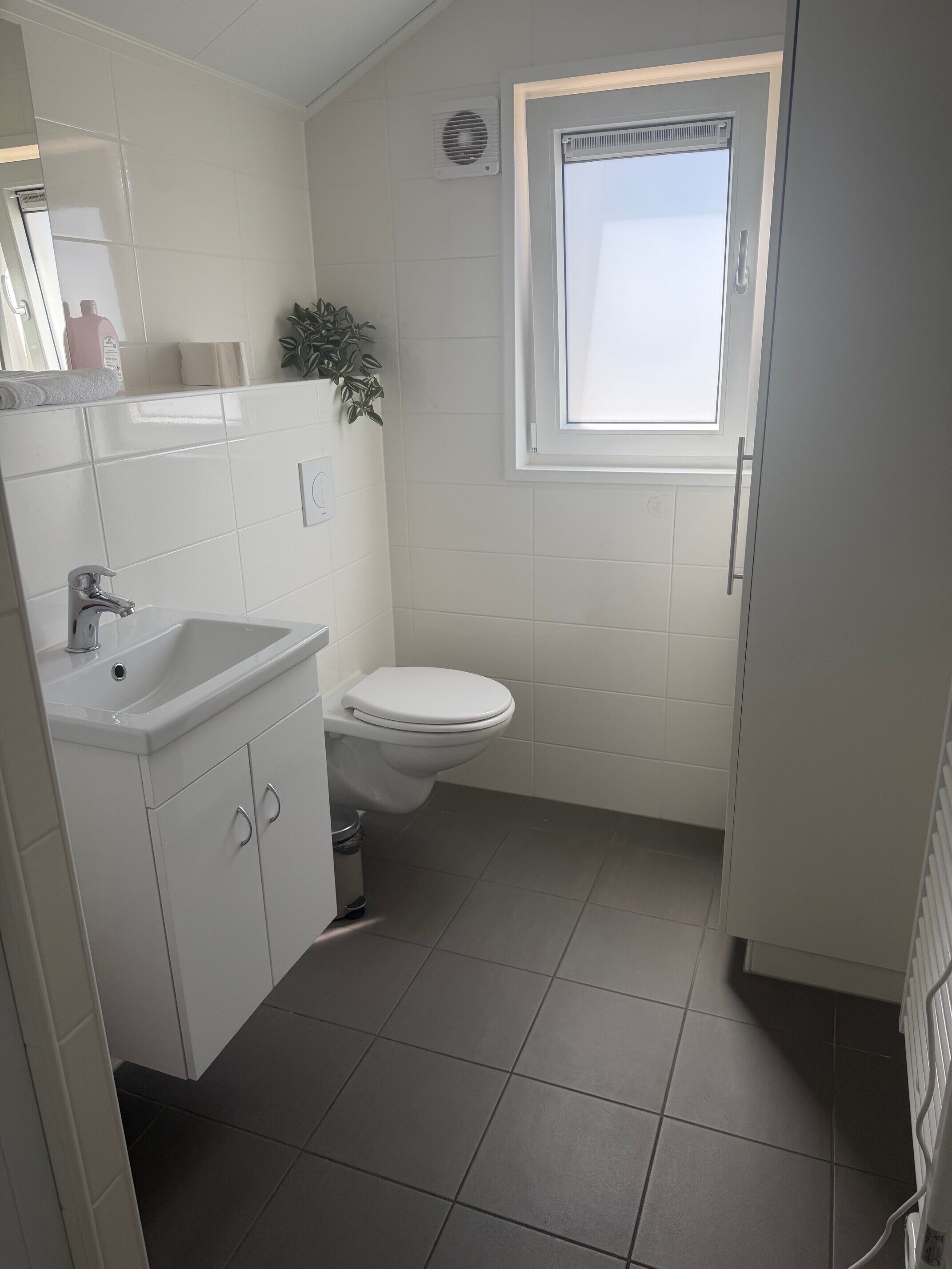 A small bathroom with a white sink, toilet, and a window.