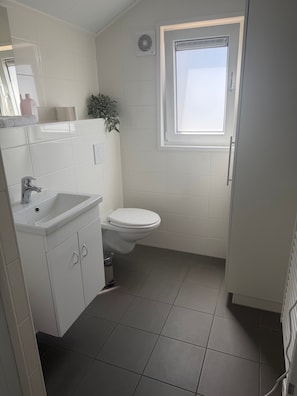 A small bathroom with a white sink, toilet, and a window. - Tiny Home “House K116” with Private Terrace, Wi-Fi & Air Conditioning (Röbel)