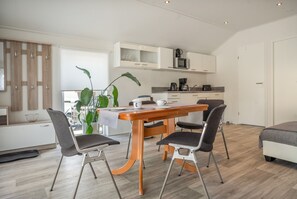 Eine moderne Küche mit weißen Schränken, einer Mikrowelle und einer Kaffeemaschine. Ein Esstisch mit Stühlen und einer Pflanze sind ebenfalls vorhanden.