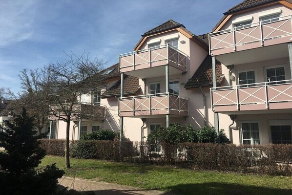 Een woongebouw met meerdere balkons, een met bakstenen bestraat pad en een goed onderhouden haag.