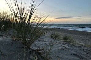 Ein Strand mit Sand und Gras im Vordergrund und dem Meer im Hintergrund.