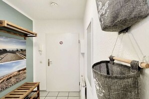 A hallway with a white door, a bench, a wall-mounted bag, and a picture of a beach. - Holiday apartment with 1 bedroom (Dierhagen)