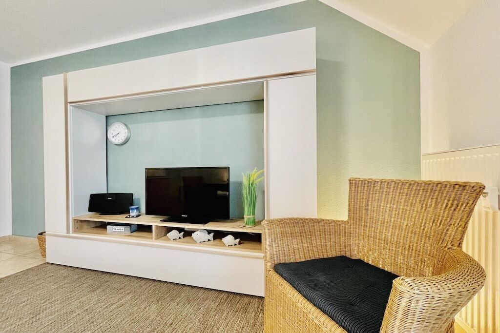 Een woonkamer met een witte tv-meubel, een flatscreen televisie, een rieten fauteuil en een kleine vis decoratie.