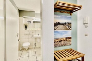 Een badkamer met toilet, wastafel en een klein schapje met een plant. Er is een houten bankje en een aan de muur bevestigd telefoon.