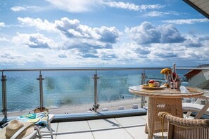 A balcony with a view of the sea, a wicker table with fruit and drinks, and a lounge chair. - Exclusive tower apartment (Burgtiefe)