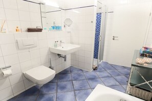 A bathroom with a white sink, a toilet, a shower with a blue shower curtain, and a white bathtub. - Exclusive tower apartment (Burgtiefe)