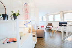 A modern living room with a sofa, a coffee table, a TV, and a bookshelf. - Exclusive tower apartment (Burgtiefe)