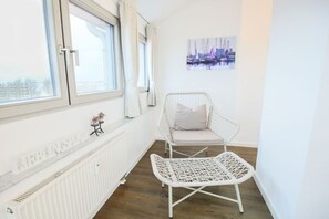 A white wicker chair with a cushion, a white radiator, and a window with curtains. - Exclusive tower apartment (Burgtiefe)