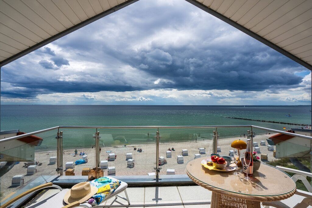 En balkon med udsigt over stranden, et bord med hat, solbriller og en flaske.