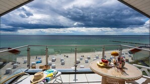 Un balcón con vista a la playa, una mesa con un sombrero, gafas de sol y una botella.