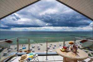 A balcony with a view of the beach, a table with a hat, sunglasses, and a bottle. - Exclusive tower apartment (Burgtiefe)