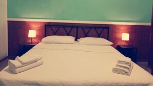 Een netjes opgemaakt bed met kussens en opgevouwen handdoeken, twee bedlampen en een houten hoofdbord.