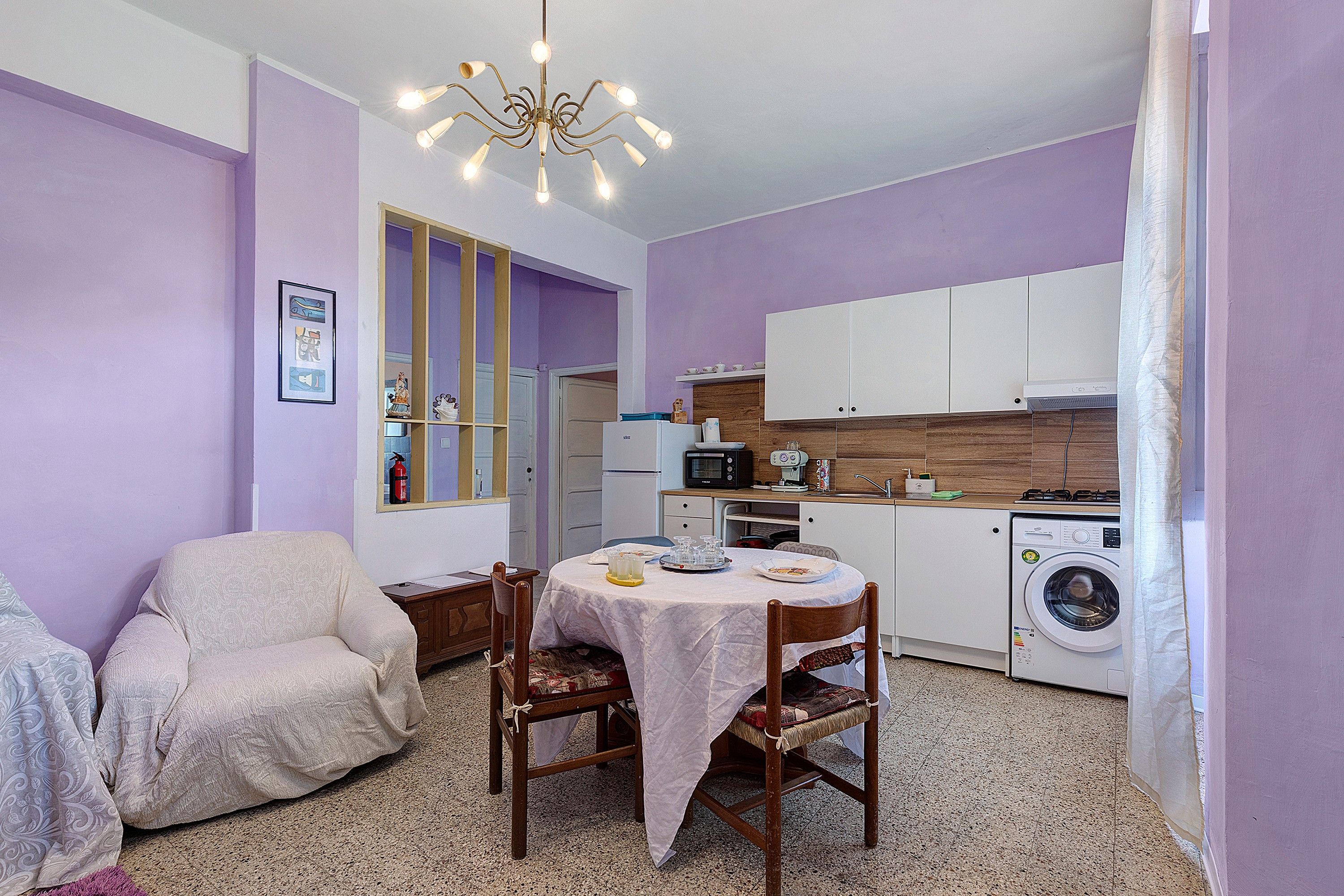 Een ruimtelijk ingerichte leefruimte met eethoek, kitchenette en een wasmachine.