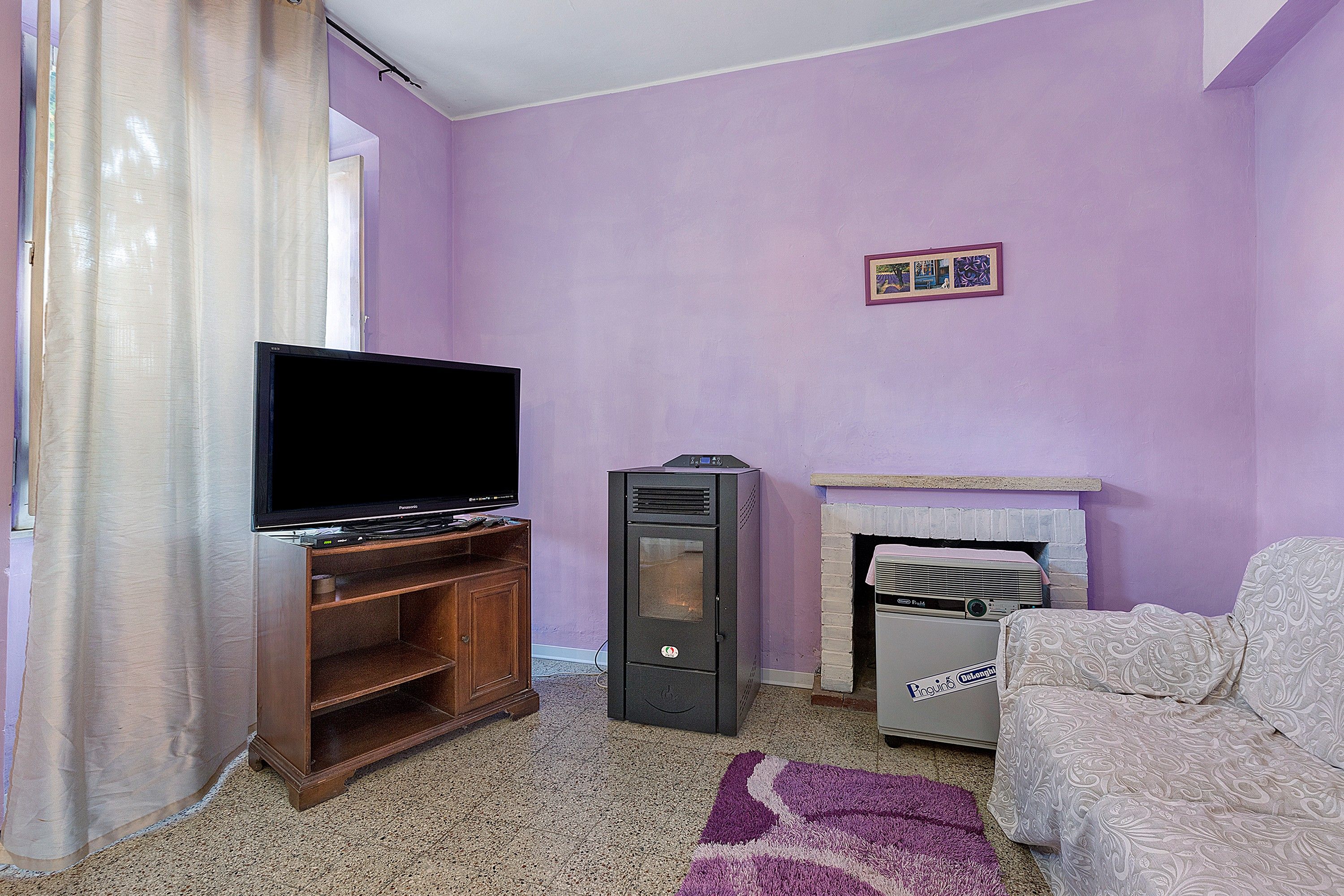 Una sala de estar con televisor sobre un mueble de madera, chimenea y alfombra estampada.
