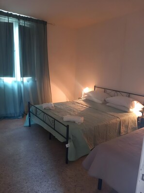 En enkeltseng med metalramme, et natbord med lampe og et vindue med let gardin.