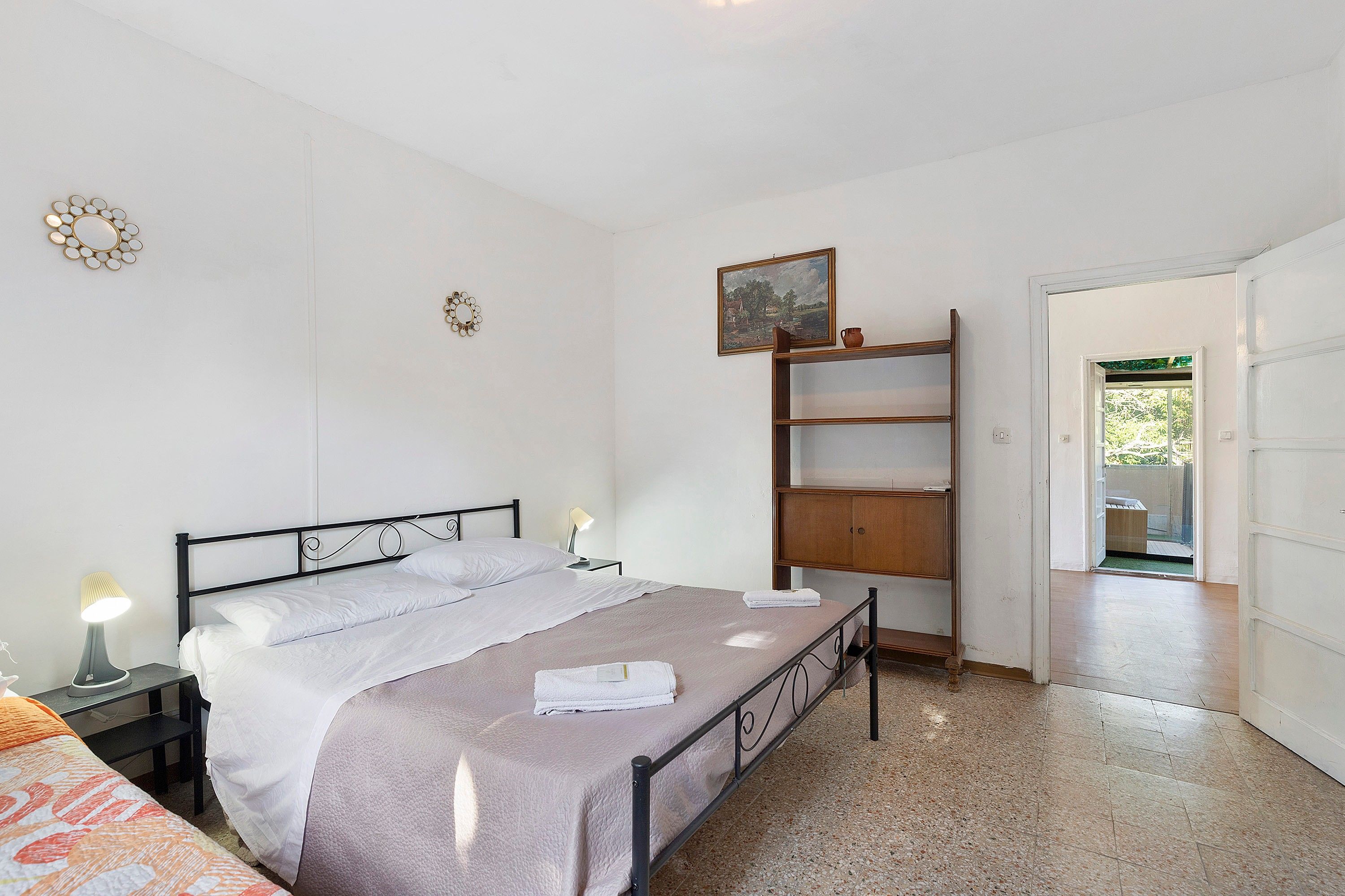 Un dormitorio con cama, mesitas de noche, estante de madera y un cuadro en la pared.
