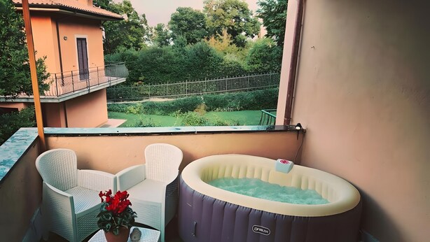 A balcony with two white wicker chairs, a small table with a potted plant, and a hot tub. - 'Rifugio Del Benessere' Apartment (Monte Compatri)