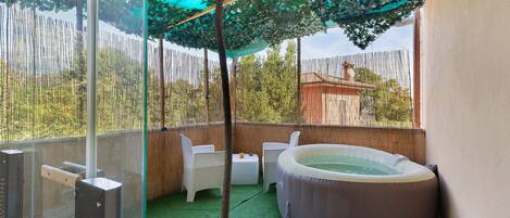 Un espacio exterior privado con jacuzzi, asientos y cerramiento de vidrio.