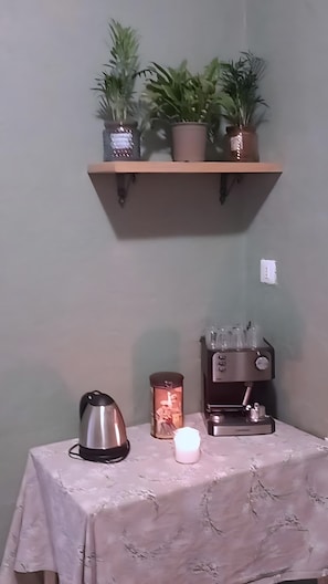 A small table with a kettle, a candle, and a coffee maker. Above the table, there is a shelf with potted plants. - 'Rifugio Del Benessere' Apartment (Monte Compatri)