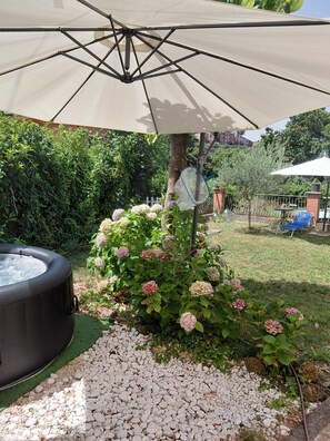 Un espace jardin aménagé avec un jacuzzi, un grand parasol et une haie d’hortensias.