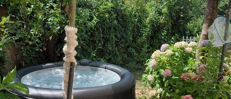 Un jacuzzi rodeado de follaje, una pérgola con toldo y un jardín de guijarros.