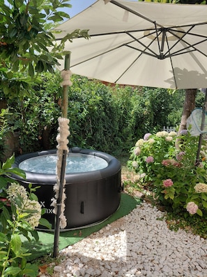 Un bain à remous entouré de verdure, une pergola avec un auvent et un jardin agrémenté de galets.