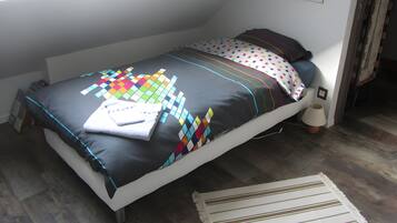 Una cama individual con un edredón colorido y una almohada blanca, una mesita de noche con una lámpara, y una ventana con vistas al exterior.