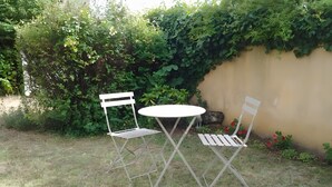Ein kleiner Sitzbereich im Freien mit zwei Metallstühlen und einem runden Tisch, umgeben von Gras und Grünpflanzen.